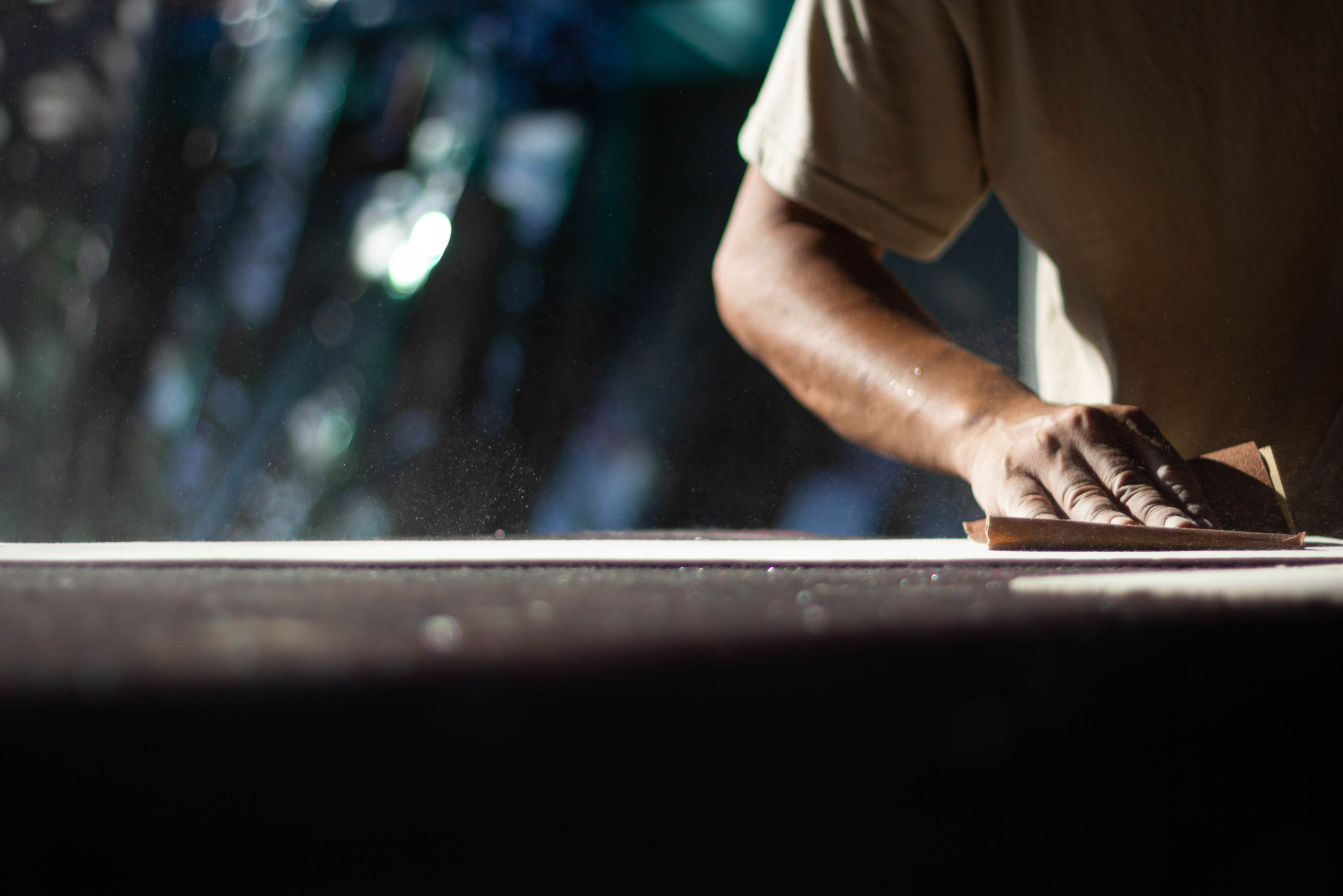 The craftsmen are using their hands to scrub the wooden boards with sandpaper which is very dusty